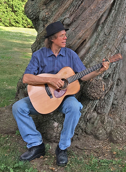 Larry playing guitar under a tree